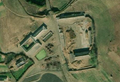 5/6 Cour de ferme (landuse=farmyard) composée de longs bâtiments, entouré d'une clôture parsemée des tas de foins, à proximité d'une route (imagerie satellite Maxar).