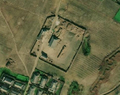 1/6 Cour de ferme (landuse=farmyard) entourée d'une clôture parsemée de tas de foins, traversée par une route (imagerie satellite Maxar).